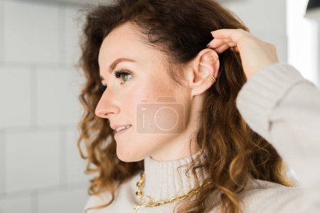 Foto de Recortado primer plano de una joven con dos asimétricas orejeras doradas. Mujer con orejeras doradas, vista lateral - Imagen libre de derechos