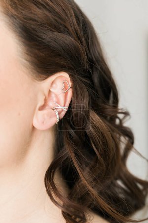 Foto de Recortado primer plano de una mujer joven con manguitos asimétricos de plata. Mujer con orejeras de metal, vista lateral. - Imagen libre de derechos