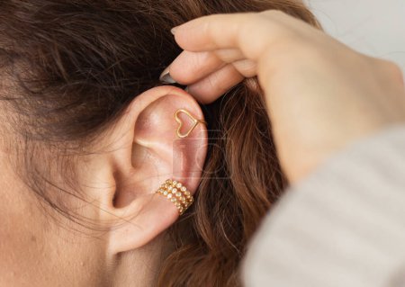 Foto de Recortado primer plano de una joven con dos asimétricas orejeras doradas. Mujer con orejeras doradas, vista lateral - Imagen libre de derechos