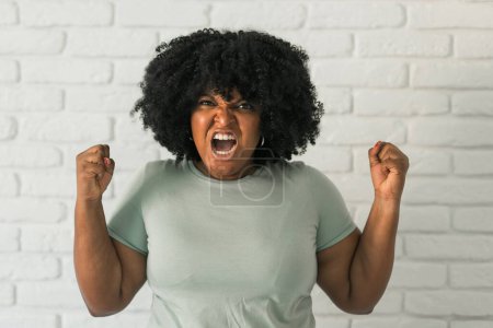 Mujer afroamericana enojada gritando sobre fondo de ladrillo. Malas emociones agresivas y síndrome premenstrual o pms