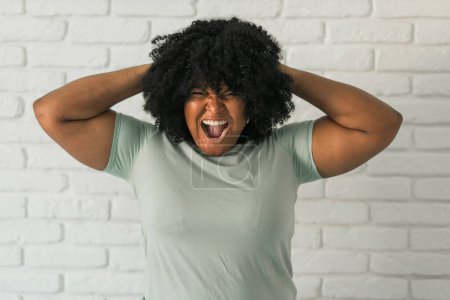 Femme afro-américaine en colère criant sur fond de brique. Mauvaises émotions agressives et syndrome prémenstruel ou pms