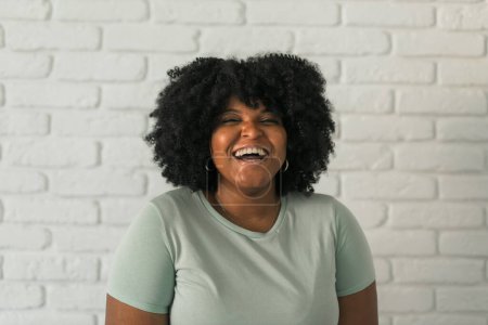 Photo for Laughing African American woman with an afro hairstyle and good sense of humor smiling and laugh on brick wall at home background. Happiness and good emotions - Royalty Free Image