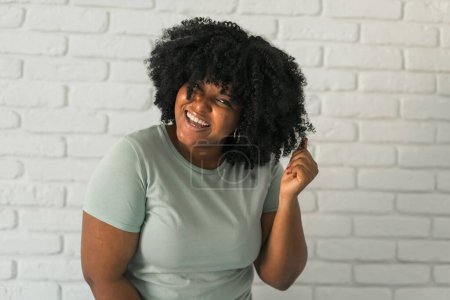 Photo for Laughing African American woman with an afro hairstyle and good sense of humor smiling and laugh on brick wall at home background. Happiness and good emotions - Royalty Free Image