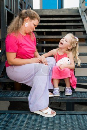 Deaf child with cochlear implant for hearing audio and aid for impairment having fun and laughs with mother outdoor in summer. Sound fitting device to help with communication listening and interaction