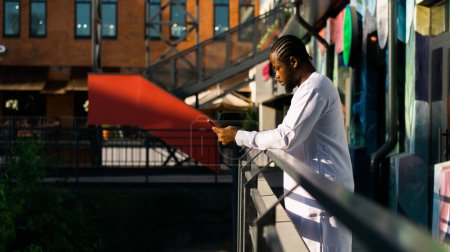 Téléchargez les photos : Millénaire génération homme afro-américain dactylographier sms extérieur 5g concept internet. Internet haut débit sur le téléphone et bavarder sur les réseaux sociaux et blog - en image libre de droit