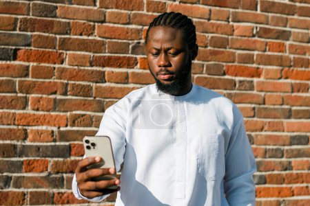 Téléchargez les photos : Un Afro-Américain vérifie son portable dans un café de rue en été. Millennial generation and gen z people. Réseaux sociaux et sortir ensemble app - en image libre de droit