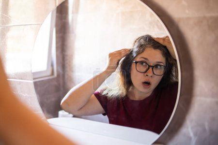 Grauhaarige überrascht kaukasische Frau mittleren Alters Blick auf graue Haare Kopf in Spiegelreflex