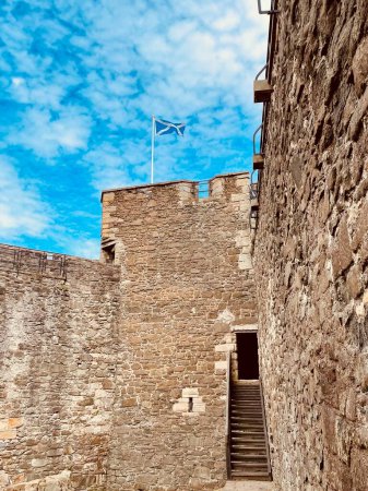 Foto de Vista desde el lado del Castillo de Blackness en Escocia. Imponentes paredes de piedra marrón con bandera escocesa ondeando encima y cielo azul brillante en el fondo. - Imagen libre de derechos