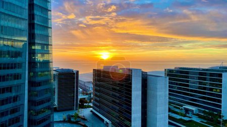 Foto de Salida del sol en Lisboa vista desde rascacielos modernos y edificios de oficinas. La salida del sol está brillando a través de nubes persistentes con el mar visible en la distancia. - Imagen libre de derechos