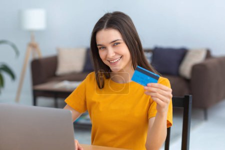 Photo for Young caucasian woman hold bank credit card, shopping online using laptop computer, buying goods or ordering online. Female holding a bank credit card in his hands and smiles friendly at the camera - Royalty Free Image