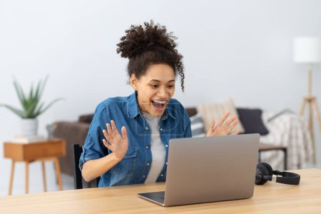 Photo for Portrait of excited young African American woman celebrating success while sitting with laptop at home or office. Happy female freelancer working in coworking space having good news - Royalty Free Image