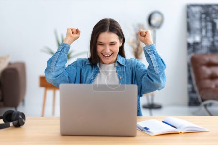 Photo for Portrait of excited young caucasian woman celebrating success while sitting with laptop at home or modern office. Happy female freelancer working in coworking space having good news - Royalty Free Image