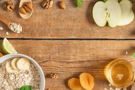 Photo for Breakfast food table. Frame of ingredients for cooking healthy breakfast. Oatmeal, dried and fresh fruits, honey and nuts on wooden table top view - Royalty Free Image