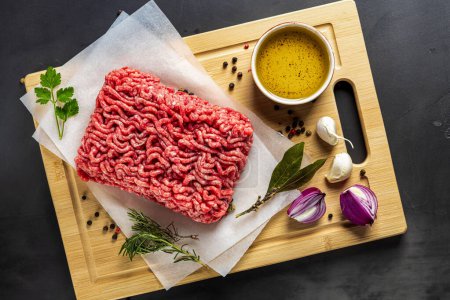 Photo for Fresh raw ground beef on cutting board on dark background with ingredients for cooking top view - Royalty Free Image