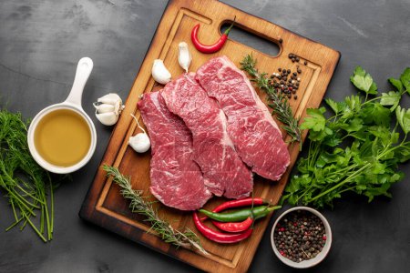 Photo for Fresh raw beef meat on cutting board on dark background with ingredients for cooking top view - Royalty Free Image
