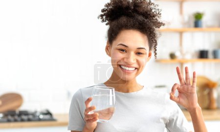 Photo for Healthy lifestyle concept. Young woman holding glass of fresh clean water looks at camera, smiles friendly. Healthy African american female follow healthy lifestyle - Royalty Free Image