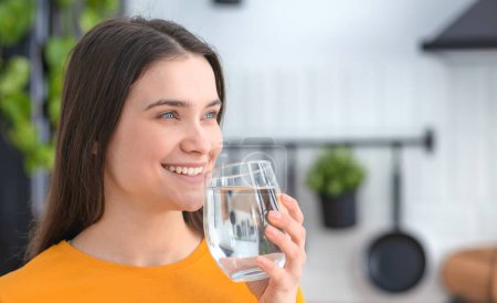 Photo for Healthy lifestyle concept. Portrait female drinking still water standing at home in the kitchen. Young smiling caucasian woman holding a glass of clean fresh water - Royalty Free Image