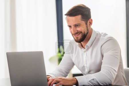 Photo for Successful businessman working using computer laptop sitting at the workplace in modern office. Bearded man entrepreneur in white shirt typing on keyboard, smiling - Royalty Free Image