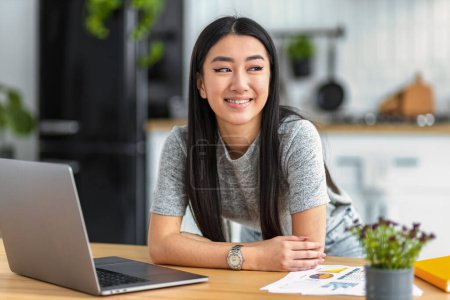 Photo for Confident happy female freelancer working from home remotely. Happy Asian woman looking away thinking of something nice - Royalty Free Image