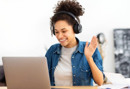 Photo for Happy African American female student in headphones using laptop computer having video call sitting in modern office or home, learning language. Freelancer working remotely, discussion something - Royalty Free Image