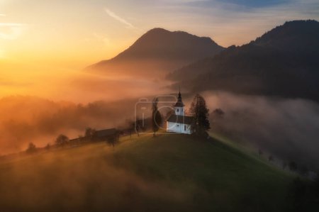 Photo for Aerial drone view of small beautiful church on a mountain in Slovenia in the rays of the sun at dawn. Beautiful autumn morning landscape - Royalty Free Image