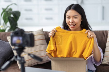 Photo for Happy woman freelancer unpacking box of clothes on camera. Young Asian female freelancer blogger - Royalty Free Image