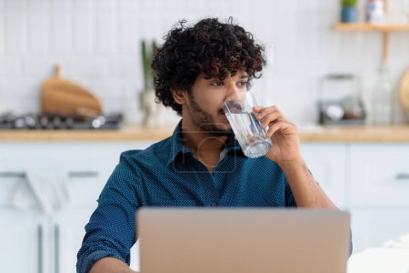Photo for Portrait of male freelancer or employee with glass fresh water sitting at workplace, coworking. Smiling Asian man using laptop computer, working at home - Royalty Free Image