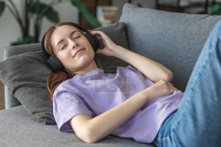 Photo for Relax at home, positive thinking. Happy young woman lying at home on the couch with headphones listening to her favorite music and thinking about something good, smiling - Royalty Free Image