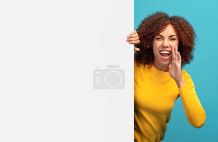 Photo for Discount black friday or sale concept. Young happy African American woman peeking out from empty white board and holding her hands near her mouth scream - Royalty Free Image