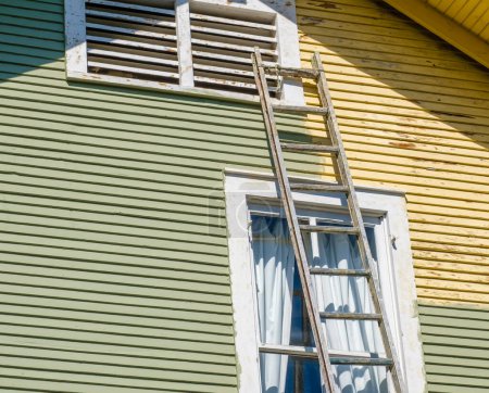 Téléchargez les photos : Échelle appuyée contre une maison historique avec un côté fraîchement peint (vert) et l'autre côté pas (jaune)) - en image libre de droit