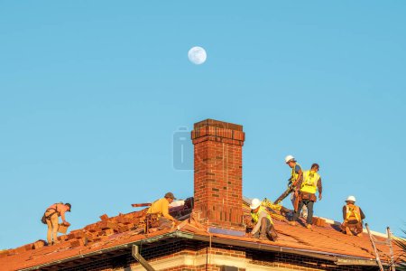 Téléchargez les photos : New Orleans, LA, USA - JANUARY 4, 2023: Workers replacing roofing tiles on a roof with the moon in the background - en image libre de droit