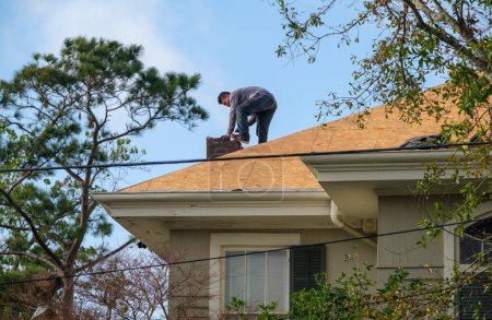 Téléchargez les photos : NEW ORLEANS, LA, USA - DECEMBER 31, 2021: Worker demolishing chimney as part of roof renovation on residential rooftop - en image libre de droit