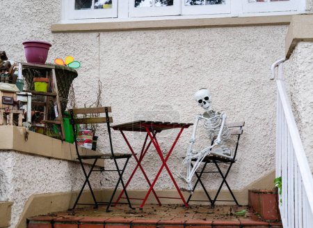 Téléchargez les photos : NEW ORLEANS, LA, USA - JANUARY 2, 2023: Skeleton (Halloween decoration) sitting in a folding chair next to a folding table on a front porch - en image libre de droit