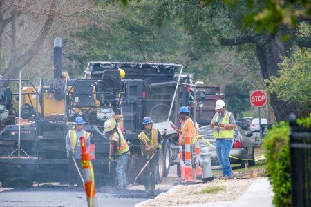 Photo for NEW ORLEANS, LA, USA - FEBRUARY 20, 2023: Workers spread hot, smoking asphalt on road surface behind heavy equipment during street repair project in Uptown Neighborhood - Royalty Free Image