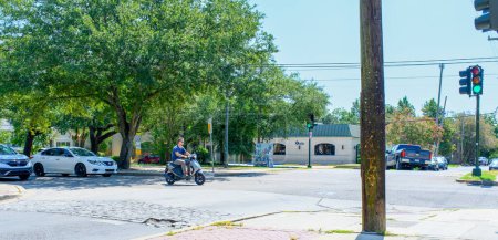 Téléchargez les photos : NOUVELLE-ORLÉANS, LA, ÉTATS-UNIS - 19 AOÛT 2023 : Un homme sans casque allume un feu rouge sur son scooter à une intersection pendant les heures de pointe dans le quartier Carrollton - en image libre de droit