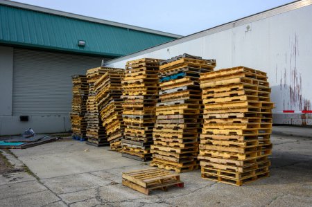 Five columns of stacked wooden pallets and large trailer at a warehouse loading dock in an industrial park in Jefferson Parish, Louisiana, USA