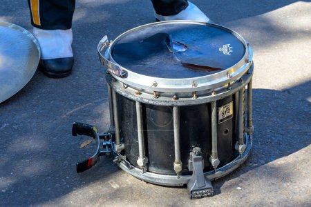Téléchargez les photos : NEW ORLEANS, LA, USA - FEBRUARY 13, 2024: Selective focus of tom-tom drum on the ground with shoes of drummer and cymbal blurred in the background on Mardi Gras parade route - en image libre de droit