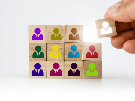 Foto de A hand placing a wooden block with colorful people icon onto many others, putting the right man into the right position, HR concept, recruitment, human resources and management - Imagen libre de derechos