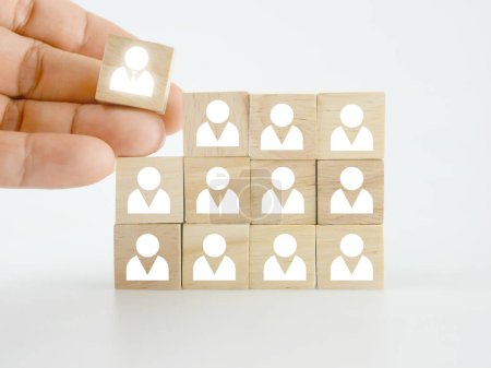 Foto de A hand placing a wooden block with people icon onto many others, putting the right man into the right position, HR concept, recruitment, human resources and management - Imagen libre de derechos