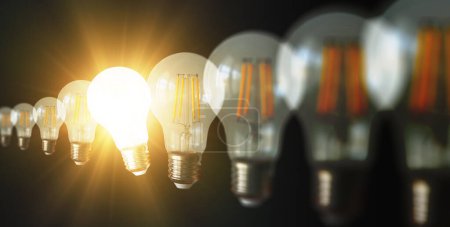 Téléchargez les photos : Une ampoule lumineuse ou rayonnante parmi d'autres ampoules non allumées sur un fond sombre représente de nouvelles idées, innovation, créativité, compréhension, connaissance et inspiration. - en image libre de droit