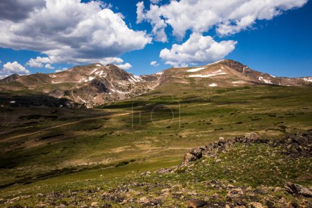Photo for The Rocky Mountains stand tall in all their majesty against a backdrop of blue sky and white clouds, with a lush green grassy foreground adding to the scenic beauty. This natural wonder, spanning over 3000 miles from New Mexico to British Columbia, i - Royalty Free Image