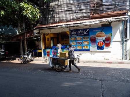 Photo for Man pushing his cooking cart past a local pastry shop on N Sathon Road by Saphan Taksin in Bangkok, Thailand. - Royalty Free Image