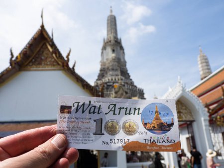 Téléchargez les photos : Il s'agit d'un billet d'entrée de cent bahts au temple Wat Arun à Bangkok, en Thaïlande, avec les flèches emblématiques du temple en arrière-plan. Wat Arun est une destination touristique populaire, connue pour son architecture impressionnante et son importance culturelle. Visito - en image libre de droit