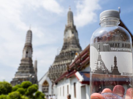 Photo for In this photo, a water bottle with a Wat Arun sticker is held up against the real temple in Bangkok, Thailand. Wat Arun, also known as the Temple of Dawn, is an iconic landmark in the city, known for its stunning architecture and cultural significanc - Royalty Free Image