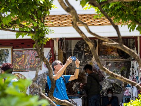 Photo for In this photo, a tourist is capturing the vibrant atmosphere of a market in Bangkok, Thailand with his phone. The market is filled with street vendors selling souvenirs and handicrafts. The bustling market provides a glimpse into the rich cultural ex - Royalty Free Image