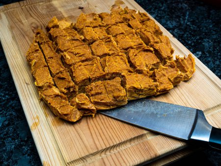 Homemade dog treats made of pumpkin, arranged on a wooden cutting block alongside a knife. The treats are a healthy and nutritious snack for dogs and are often preferred by pet owners who prefer natural ingredients.