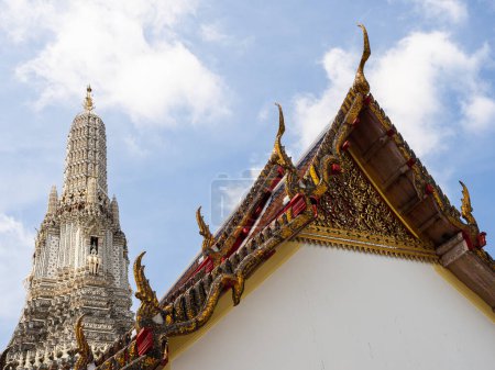 Photo for Experience the beauty and grandeur of the Wat Arun Temple in Bangkok, Thailand. The intricate red and gold roof details, set against a deep blue sky with fluffy white clouds, make for a captivating sight. This image is sure to transport you to the he - Royalty Free Image