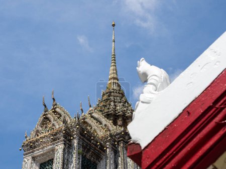 Photo for The spire of the Wat Arun Temple, Bangkok, Thailand, stands tall against the blue sky, adorned with intricate roof details in red and white. The intricate patterns and detailed craftsmanship showcase the rich cultural heritage of the temple and the c - Royalty Free Image