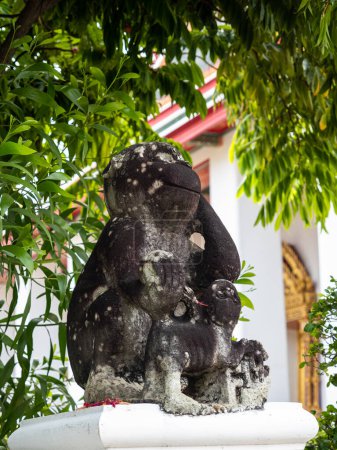 Photo for A cheerful monkey statue smiles among the greenery in front of the Wat Pho temple, a Buddhist cultural landmark in Bangkok, Thailand. - Royalty Free Image