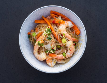 Photo for Shrimps, carrots, scallions and chili tossed with noodles in a spicy Asian sauce and presented in a white bowl. - Royalty Free Image